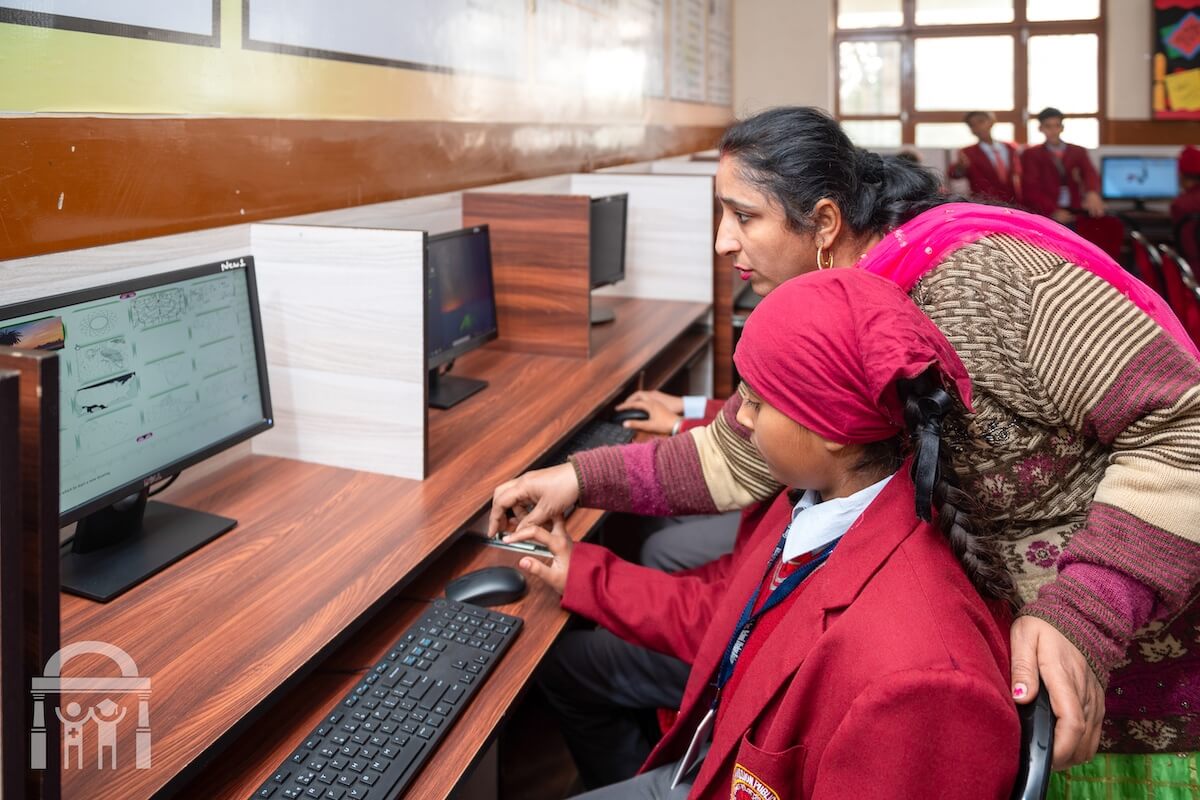 Teacher helping primary grade student in computer lab at GN Public School in Dhahan Kaleran, SBS Nagar, Punjab, India